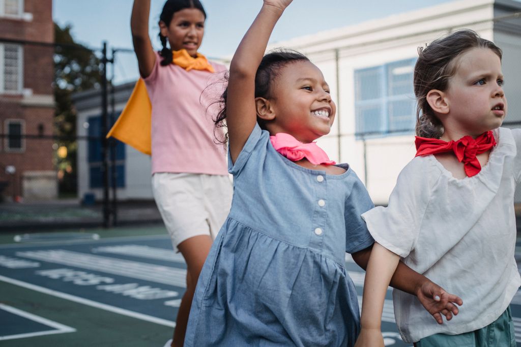 Three kids enjoying superhero play on a sunny outdoor court.