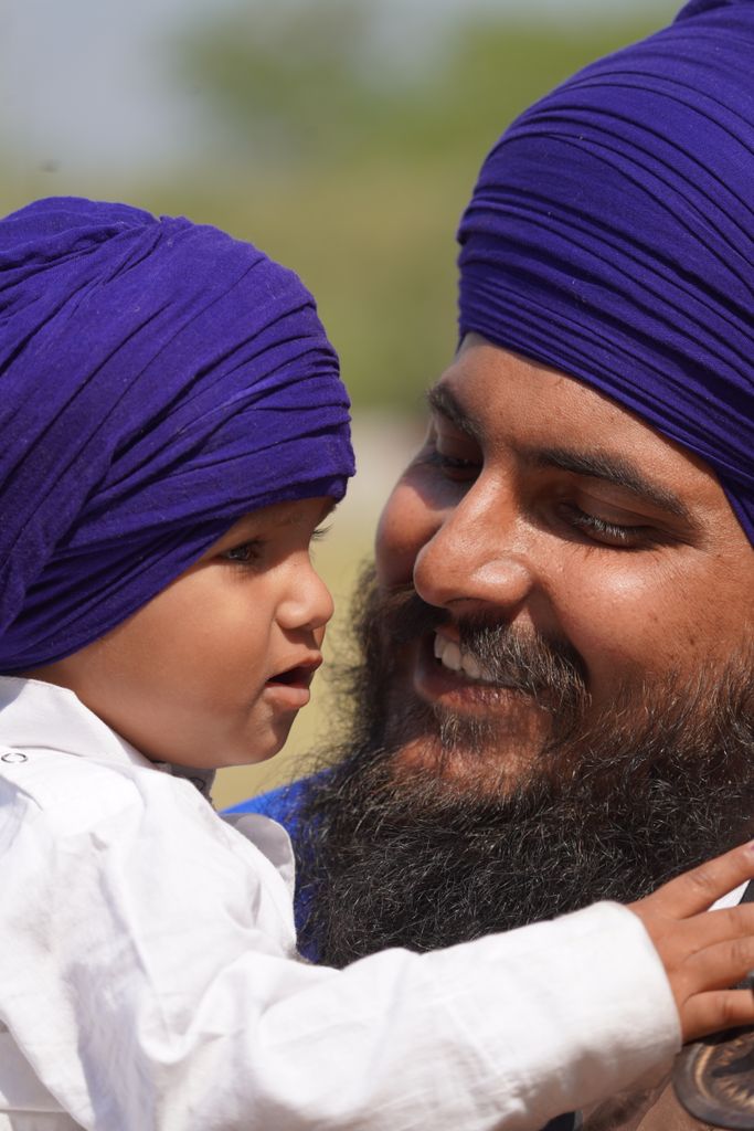 A joyful moment between a father and son wearing blue turbans outdoors.