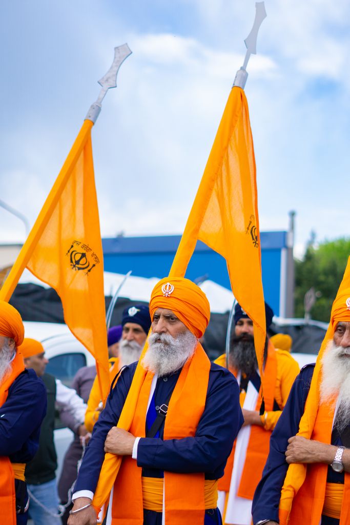 Elderly Sikh men with orange turbans leading a traditional parade holding flags outdoors.